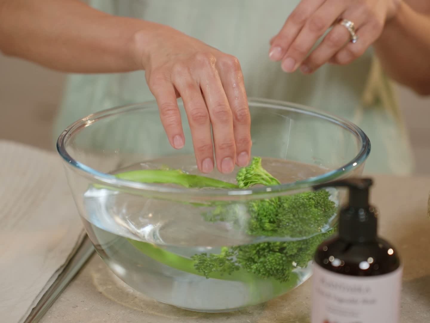 Hands adding fresh greens into a bowl of water