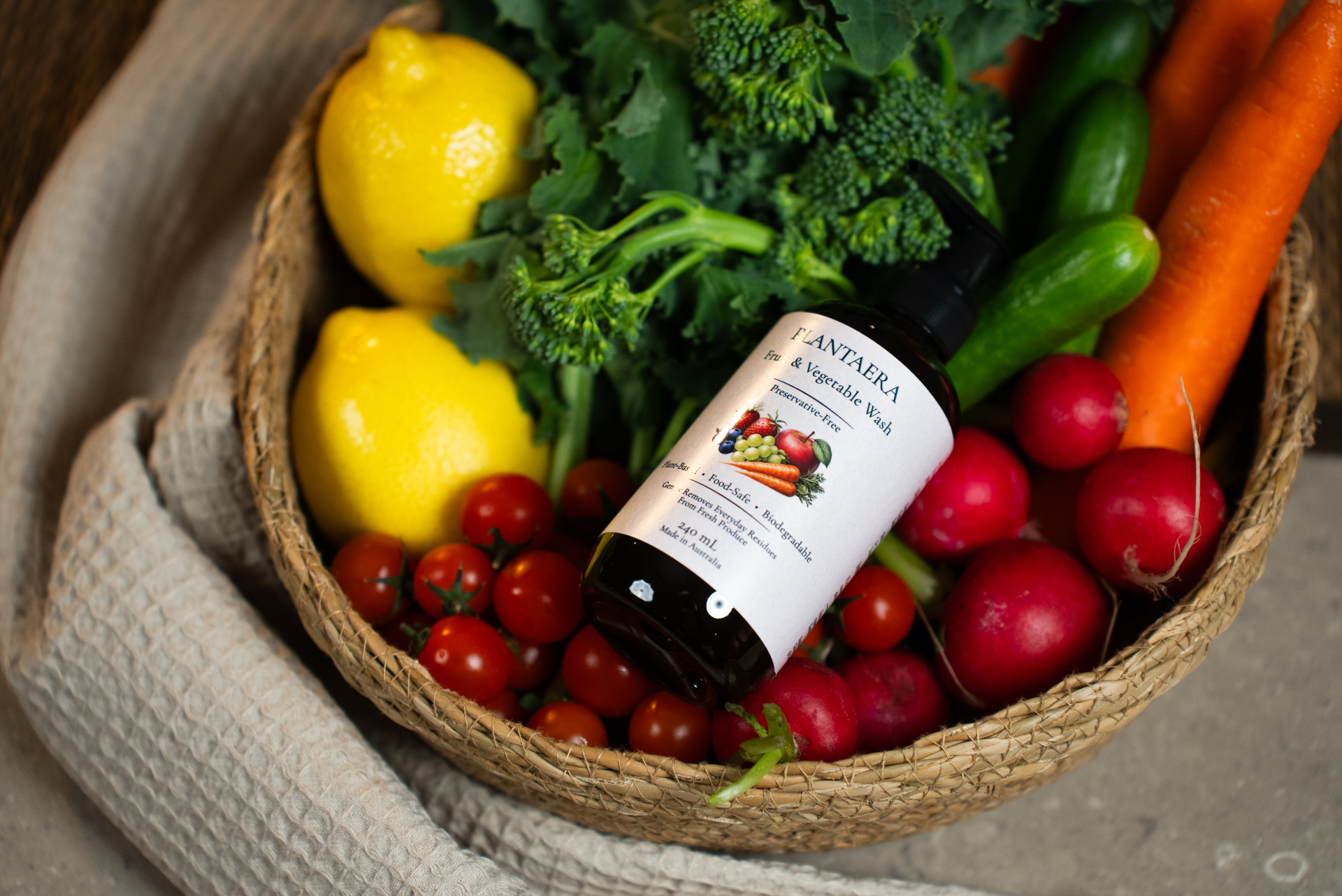 A Plantaera bottle resting in a basket of lemons, broccoli, tomatoes and radishes