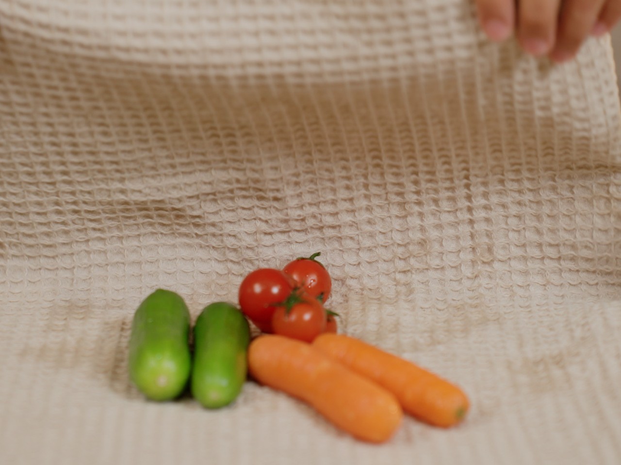 Carrots, cucumbers and tomatoes being dried on a cream waffle towel.