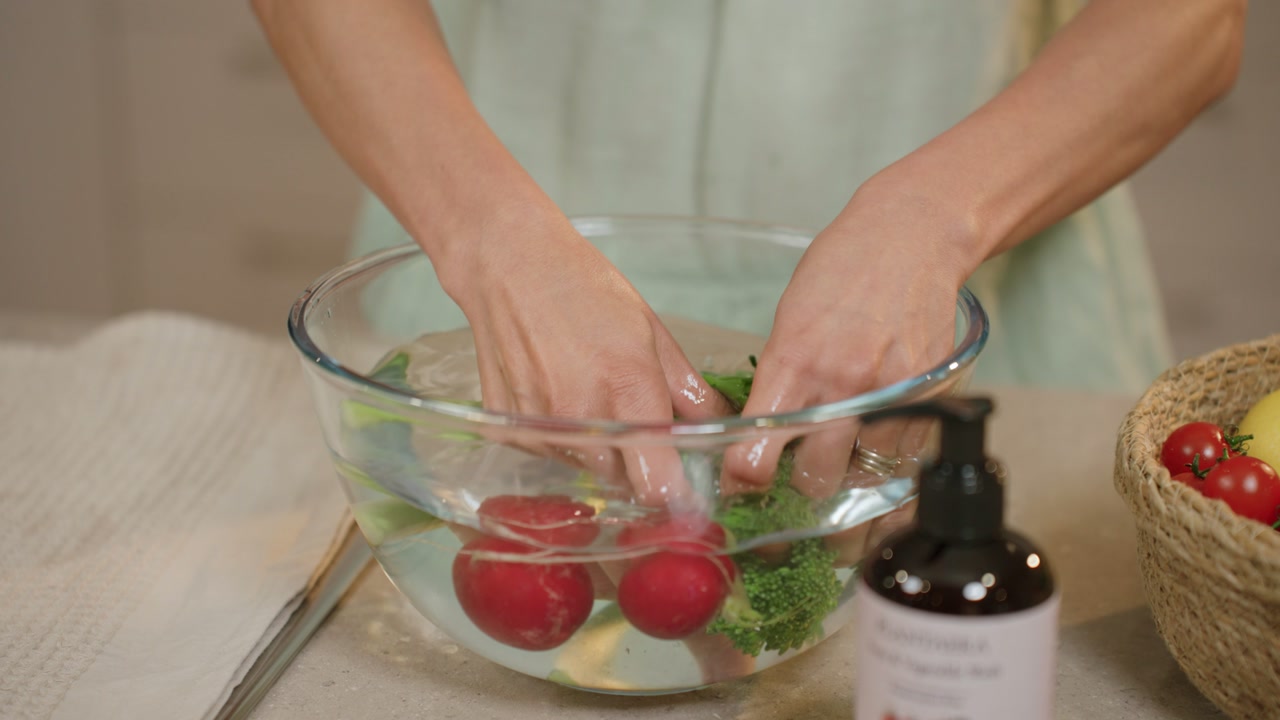 Hands gently rinsing produce in the bowl of water